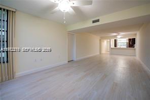 An empty living room with light-colored wood flooring, a ceiling fan, and an open kitchen — 1713 Whitehall Dr # 302, Davie FL 33324, DAVIE, FL