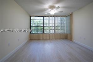 An empty room with light wood-look flooring, a ceiling fan, and large vertical-blind windows — 1713 Whitehall Dr # 302, Davie FL 33324, DAVIE, FL