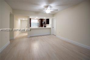 An interior view shows a living area with light wood flooring leading to a kitchen — 1713 Whitehall Dr # 302, Davie FL 33324, DAVIE, FL