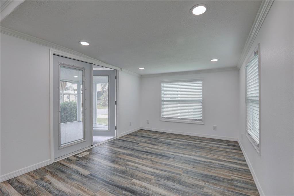 An empty room with wood-look flooring, white walls, recessed lighting, and a glass door — BAREFOOT BAY, FL