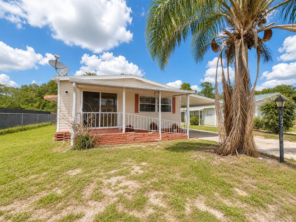 A single-story mobile home with a front porch, wheelchair ramp, and a large palm tree — 347 CANAL COURT, LAKE WALES, FL