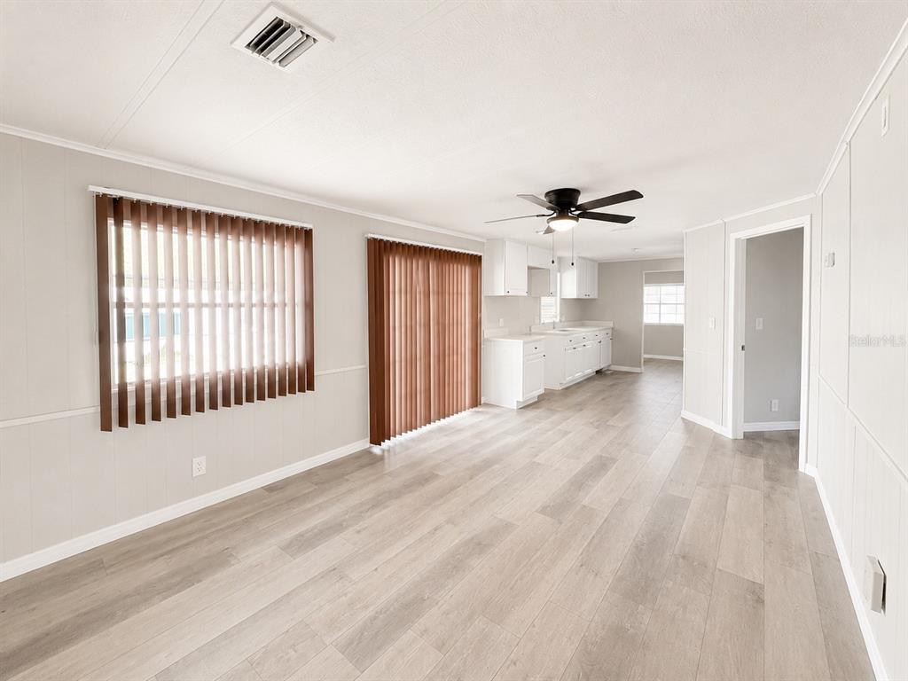 An open-concept living area features light wood-look flooring, white walls, and a kitchen beyond — 347 CANAL COURT, LAKE WALES, FL