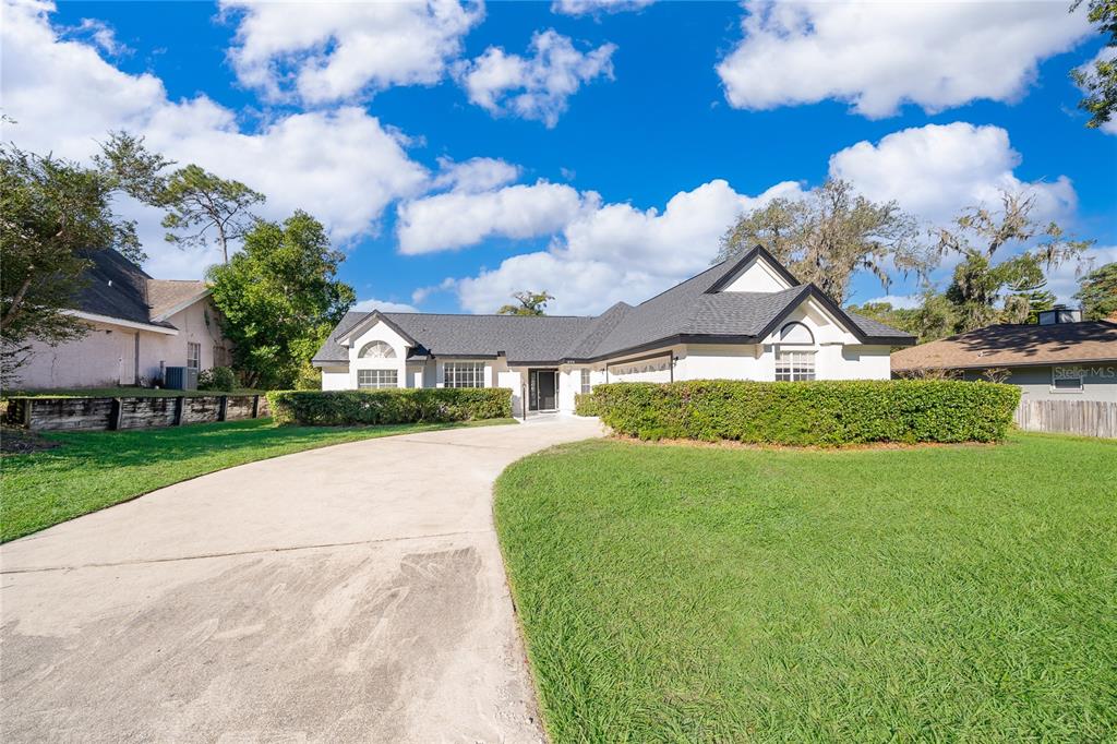A single-story house with a white exterior, dark roof, and a large front hedge — 1250 GLENMORE DRIVE, APOPKA, FL