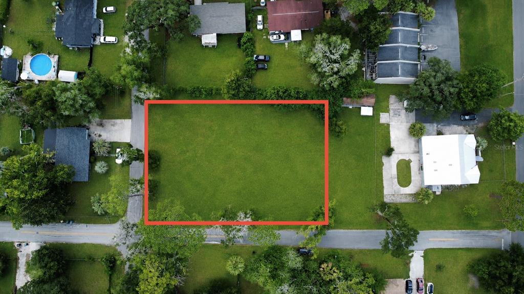 An aerial view shows a vacant rectangular lot outlined in red situated between residential properties — NW 4TH AVENUE, OCALA, FL