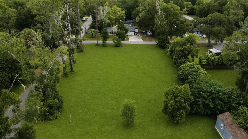 An aerial view shows a large, rectangular, grassy vacant lot surrounded by mature trees — NW 4TH AVENUE, OCALA, FL