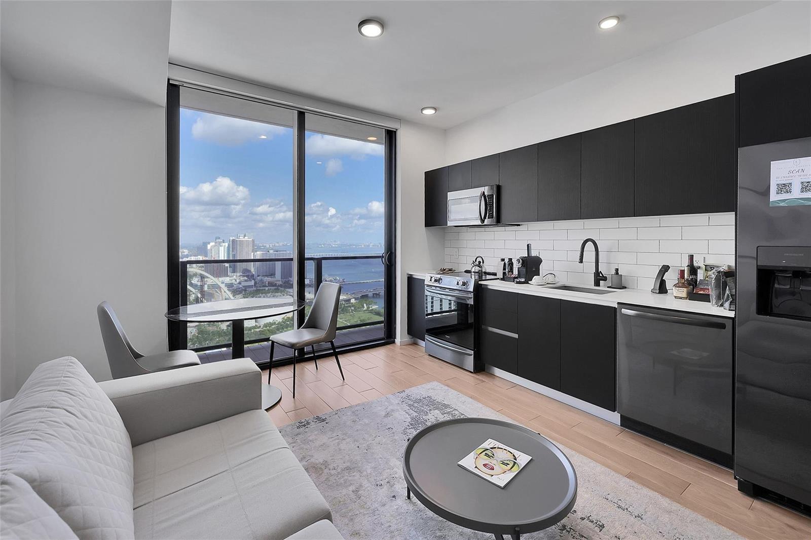 A modern apartment kitchen and living area with black cabinetry, light wood floors, and balcony — 398 NE 5th Street # 4404, Miami FL 33132, MIAMI, FL