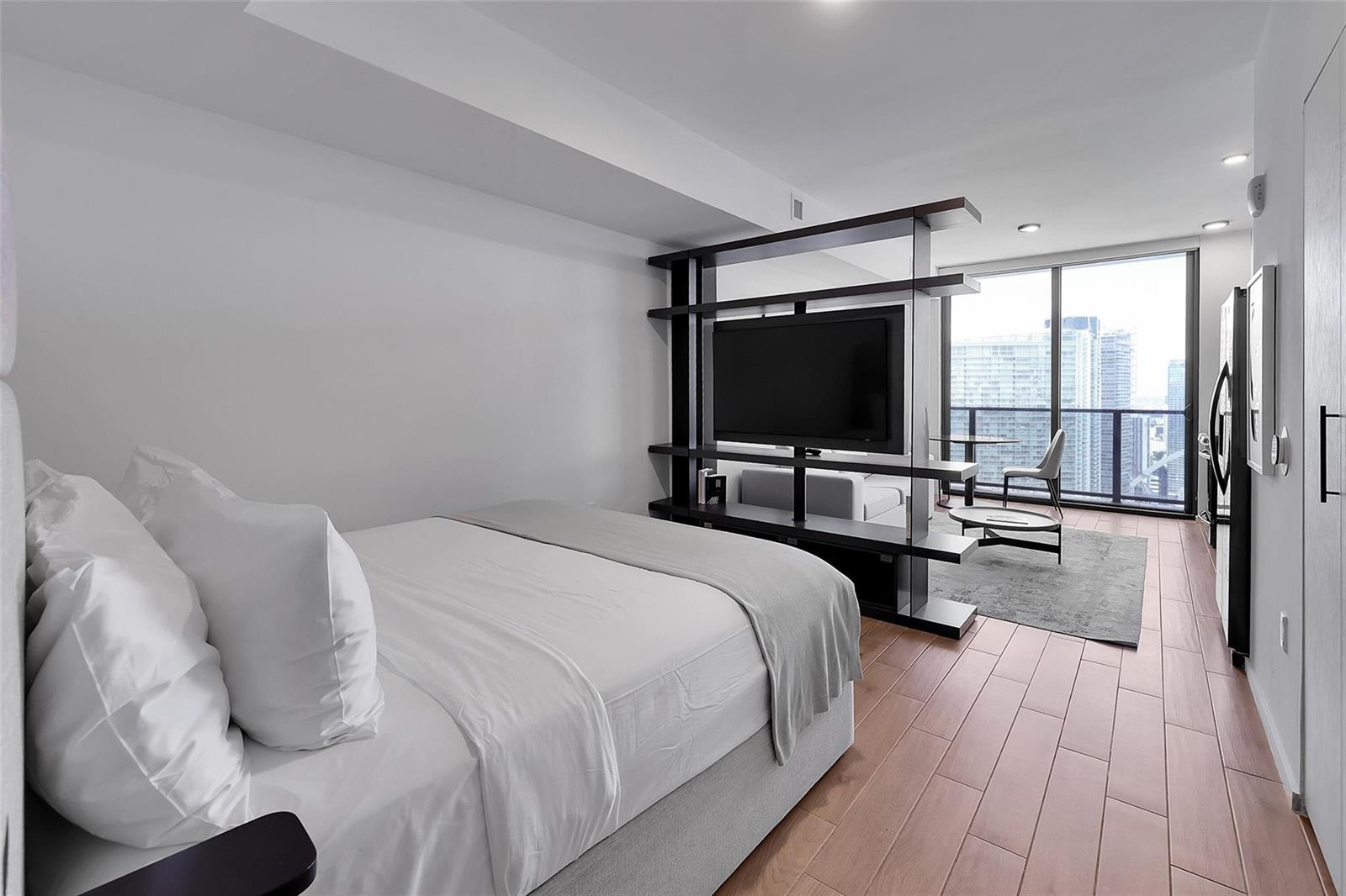 A studio apartment featuring a bed, a room-dividing shelving unit with a television, and floor-to-ceiling windows — 398 NE 5th Street # 4404, Miami FL 33132, MIAMI, FL