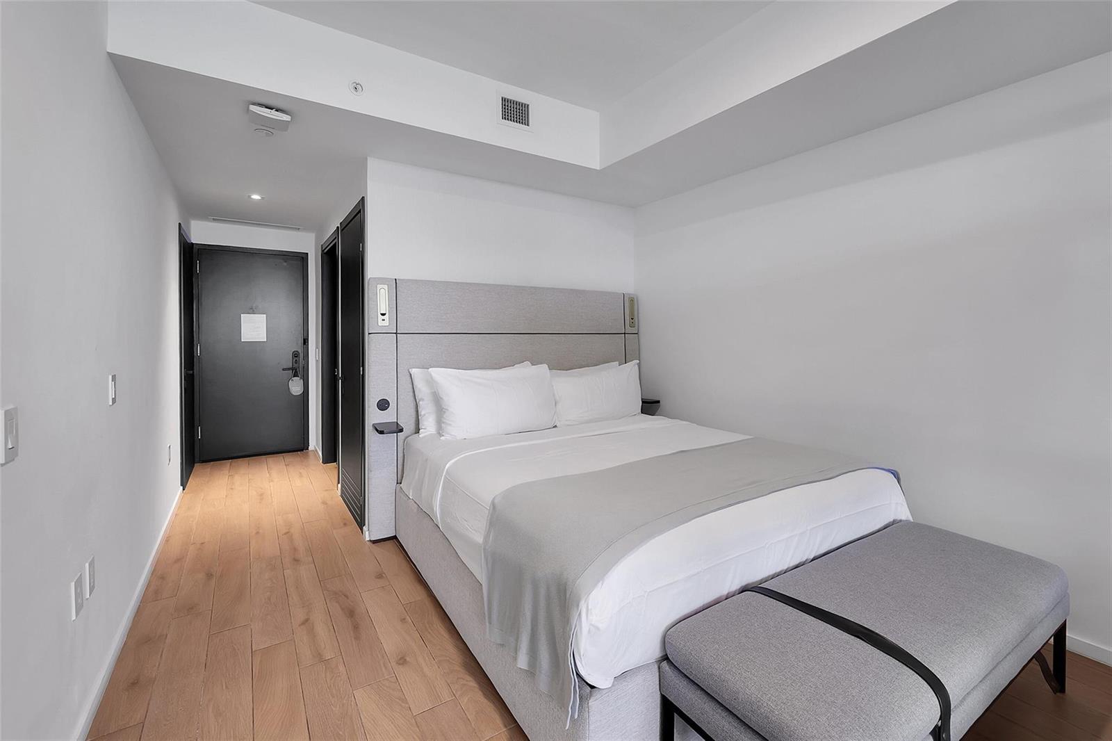 A bedroom features a queen bed with a gray headboard, a bench, and wood flooring — 398 NE 5th Street # 4404, Miami FL 33132, MIAMI, FL