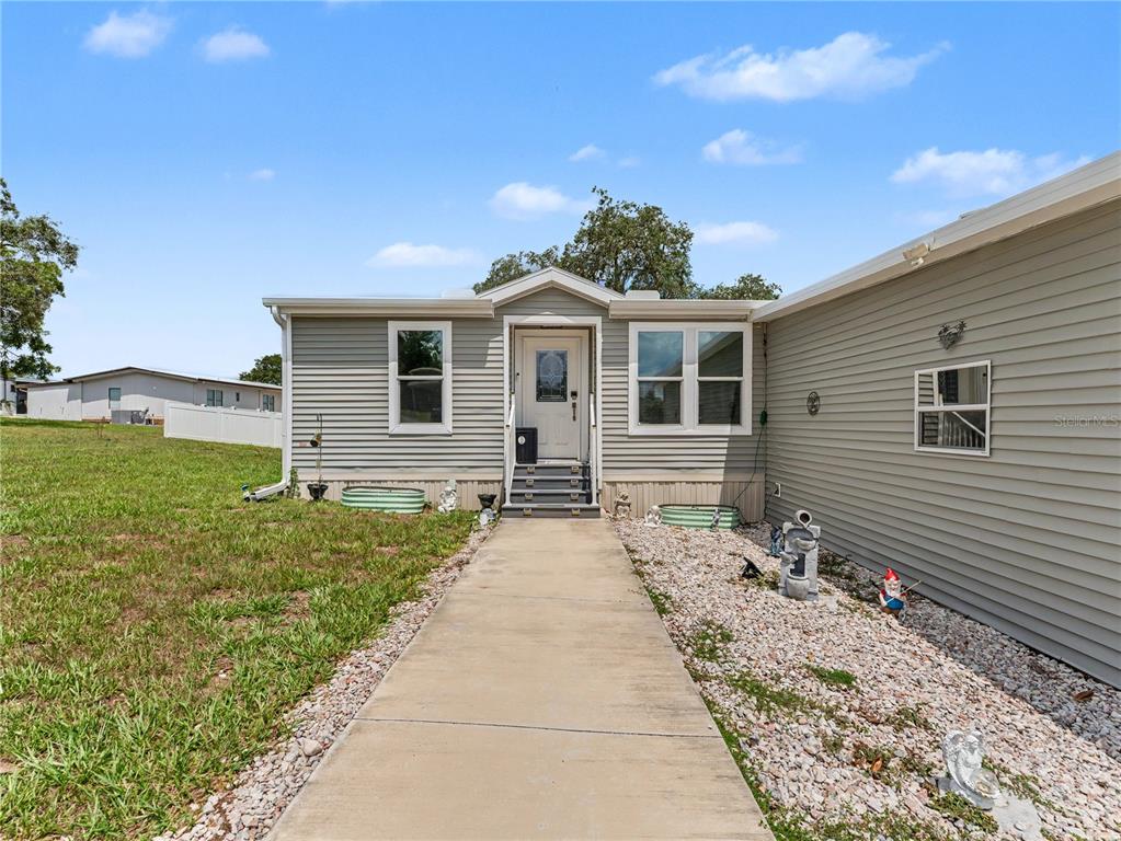 A concrete walkway leads to the front entrance of a light-gray vinyl-sided mobile home — 12532 FAIRWAY AVENUE, BROOKSVILLE, FL