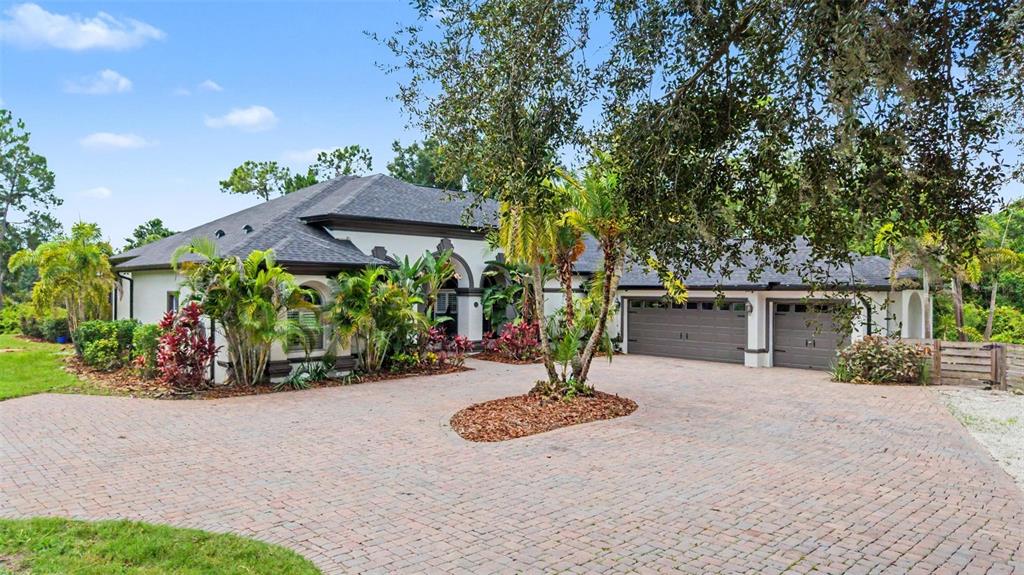A single-story house with a brick paver driveway, a three-car garage, and lush landscaping — 15532 LAKE GRACE DRIVE, ODESSA, FL