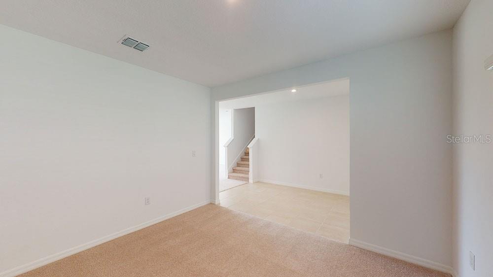 A room with beige carpet transitions into a tiled area featuring a staircase — 6753 EQUINOX LANE N, NORTH FORT MYERS, FL