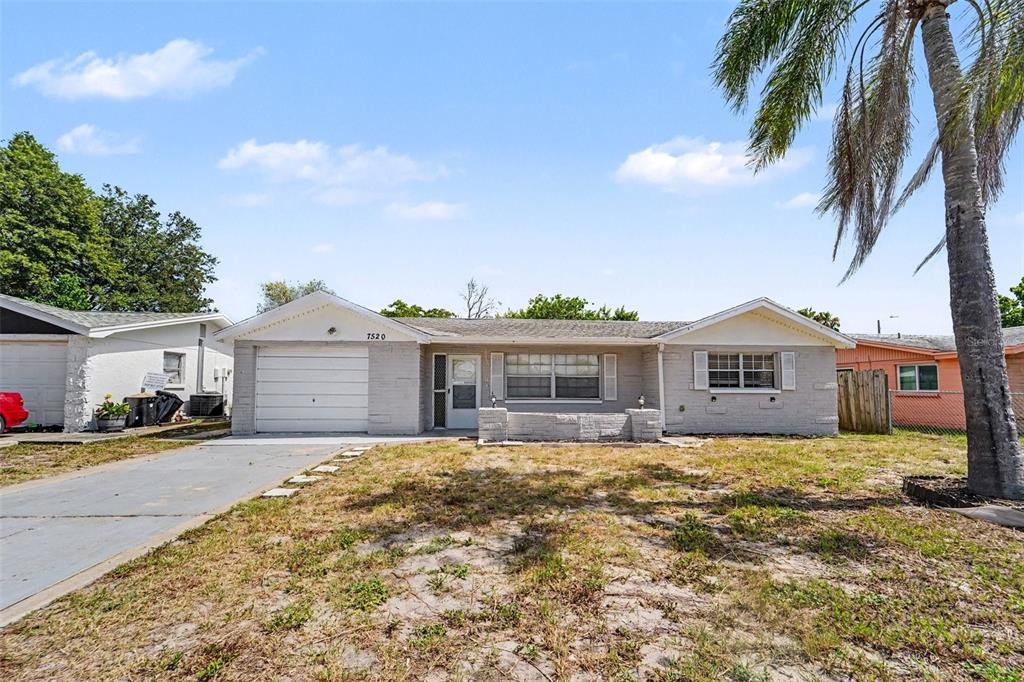 A single-story house with a light gray brick exterior, a garage, and a palm tree — 7520 CAMELOT ROAD, PORT RICHEY, FL