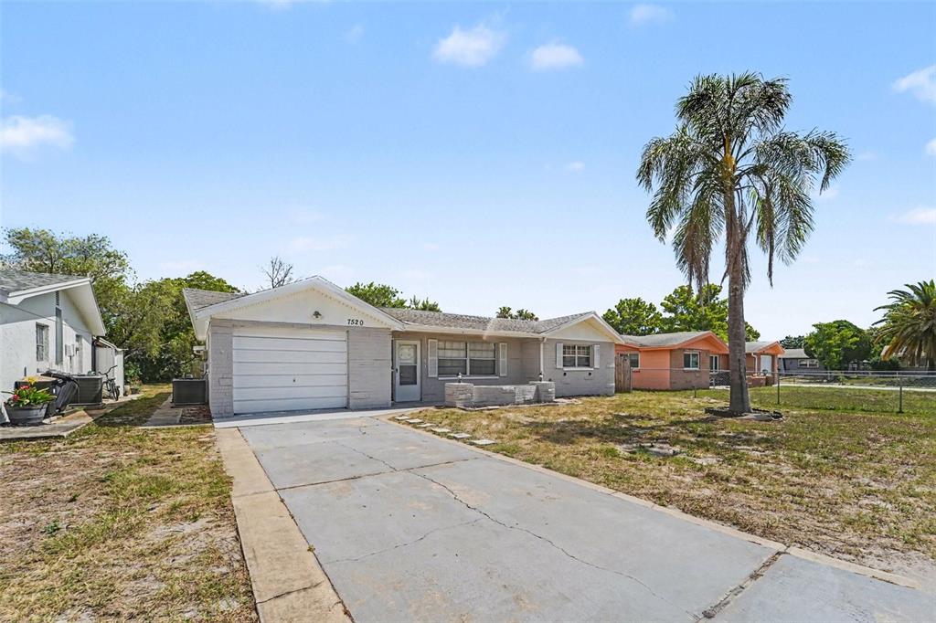 A single-story house with a gray brick exterior, a concrete driveway, and a palm tree — 7520 CAMELOT ROAD, PORT RICHEY, FL