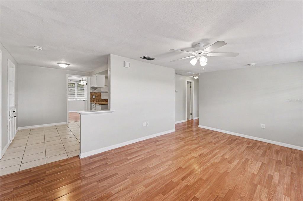 A living room with wood-look flooring connects to a tiled kitchen area with a half-wall — 7520 CAMELOT ROAD, PORT RICHEY, FL