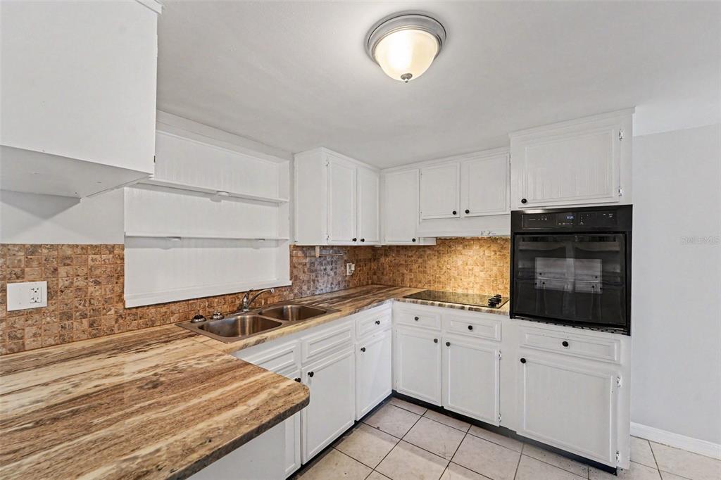 A kitchen features white cabinets, a brown patterned countertop, a tiled backsplash, and an oven — 7520 CAMELOT ROAD, PORT RICHEY, FL