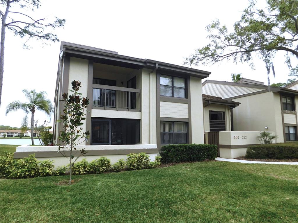 A two-story apartment building with a balcony, screened patio, and a grassy lawn — 207 WOODLAKE WYNDE UNIT 207, OLDSMAR, FL