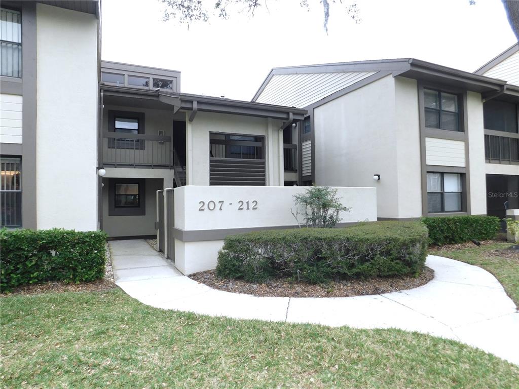 A two-story apartment building exterior features a concrete walkway leading to units 207-212 — 207 WOODLAKE WYNDE UNIT 207, OLDSMAR, FL