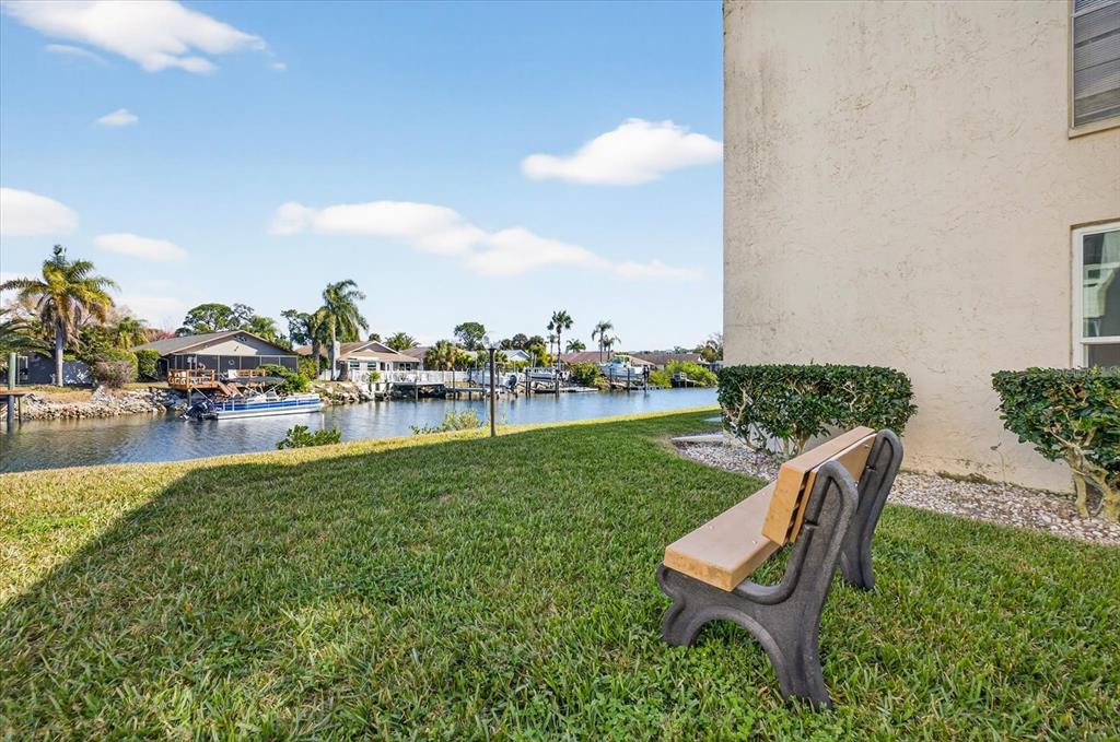 A bench sits on a grassy lawn beside a building overlooking a canal with boats — 4533 MARINE PARKWAY UNIT 203, NEW PORT RICHEY, FL