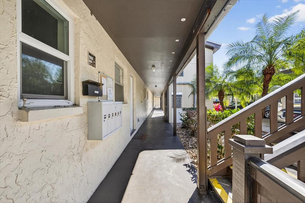 An outdoor apartment walkway features a row of mailboxes, a staircase, and palm trees — 4533 MARINE PARKWAY UNIT 203, NEW PORT RICHEY, FL