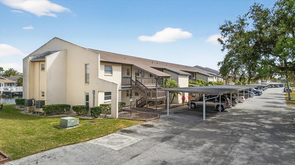 An exterior view of a multi-story apartment building with covered parking spaces and a lawn — 4533 MARINE PARKWAY UNIT 203, NEW PORT RICHEY, FL