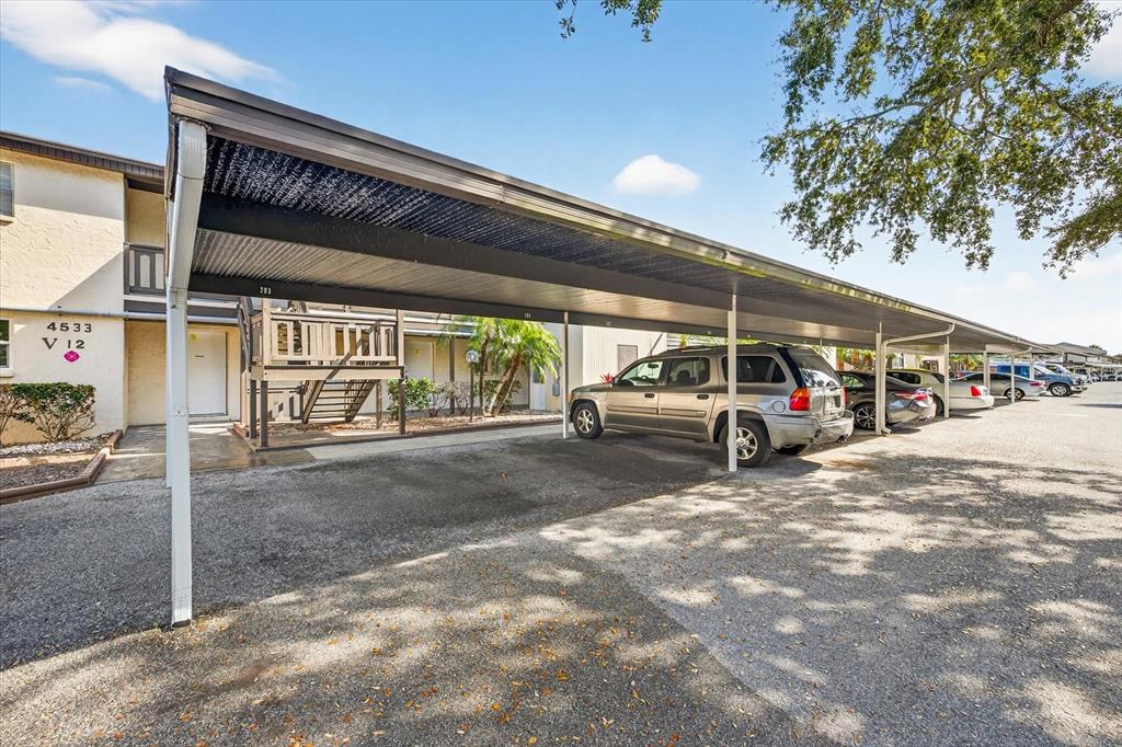 A covered parking area sits in front of a multi-story apartment building with stairs — 4533 MARINE PARKWAY UNIT 203, NEW PORT RICHEY, FL