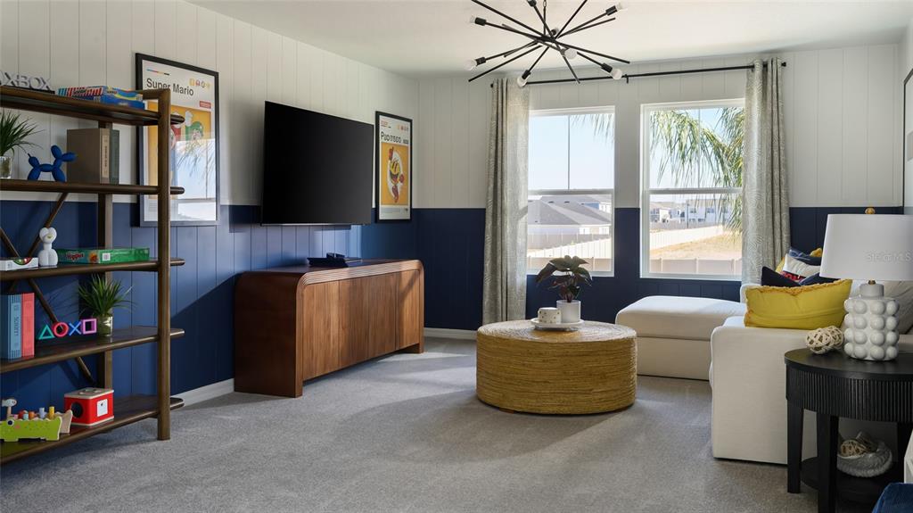 A living room features blue wainscoting, a wall-mounted television, a wooden console, and a round ottoman — 2358 STILLVIEW PASS, ZEPHYRHILLS, FL