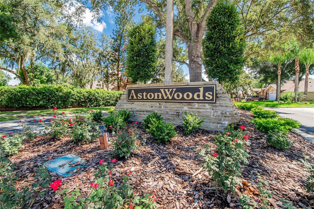 A stone monument sign for AstonWoods stands in a landscaped garden with trees and shrubs — 2704 ASTON AVENUE, PLANT CITY, FL