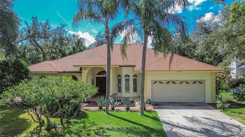 A single-story house with a brown roof, beige stucco walls, and two tall palm trees — 2704 ASTON AVENUE, PLANT CITY, FL