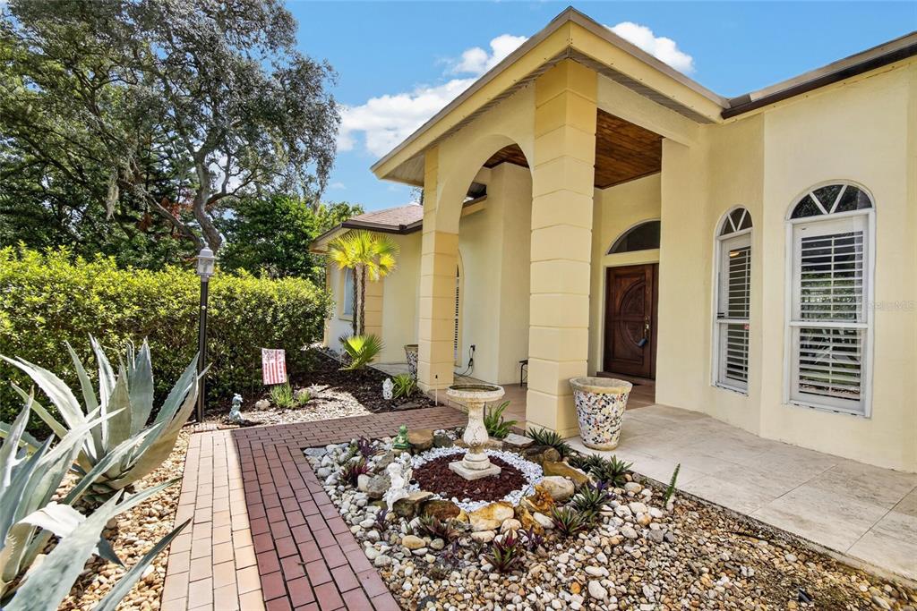 A yellow house exterior features a brick walkway, a small fountain, and a covered entryway — 2704 ASTON AVENUE, PLANT CITY, FL