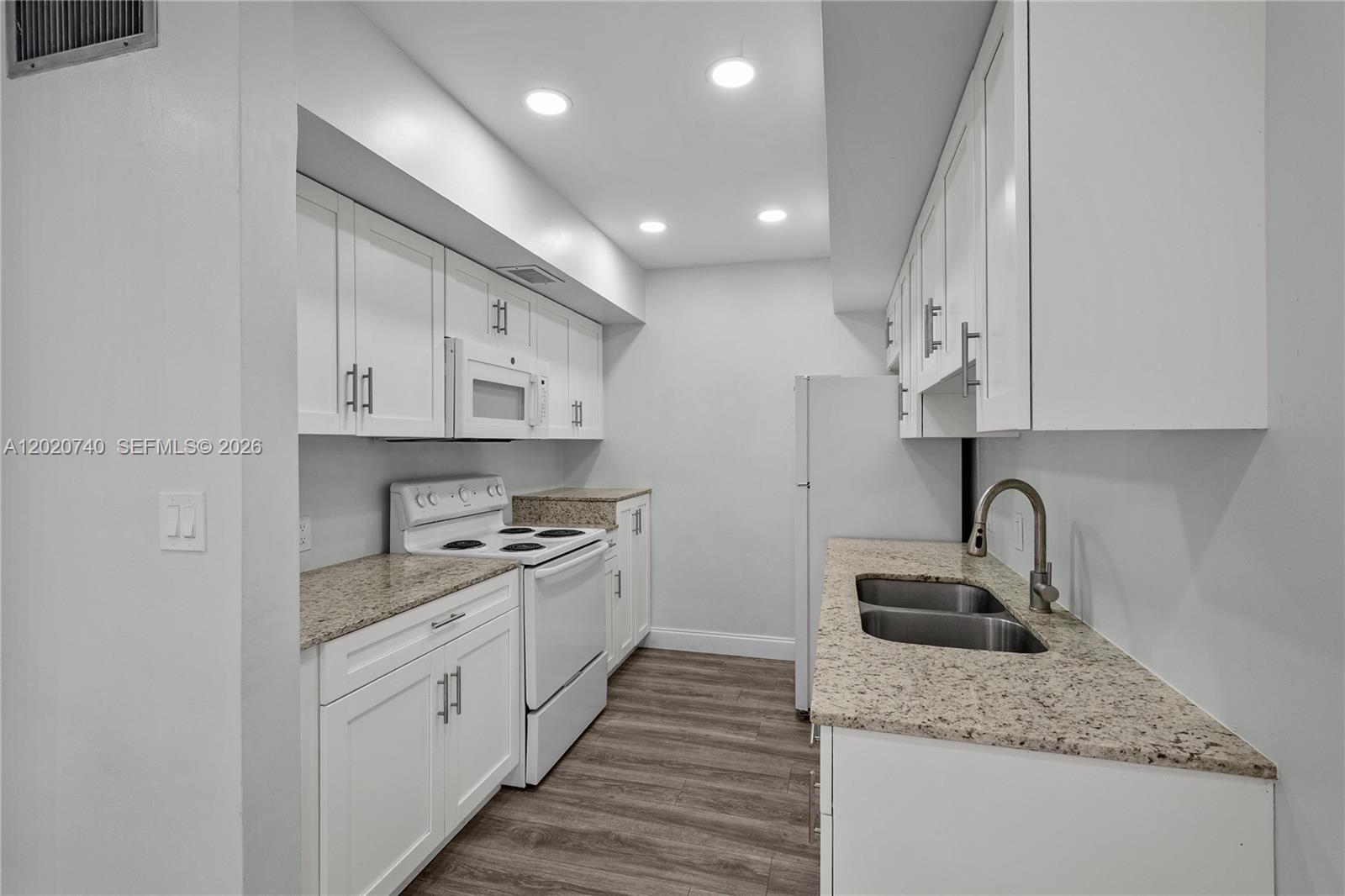 A galley kitchen features white cabinets, granite countertops, stainless steel sink, and wood-look flooring — 245 NE 191st St # 3014, Miami FL 33179, MIAMI, FL