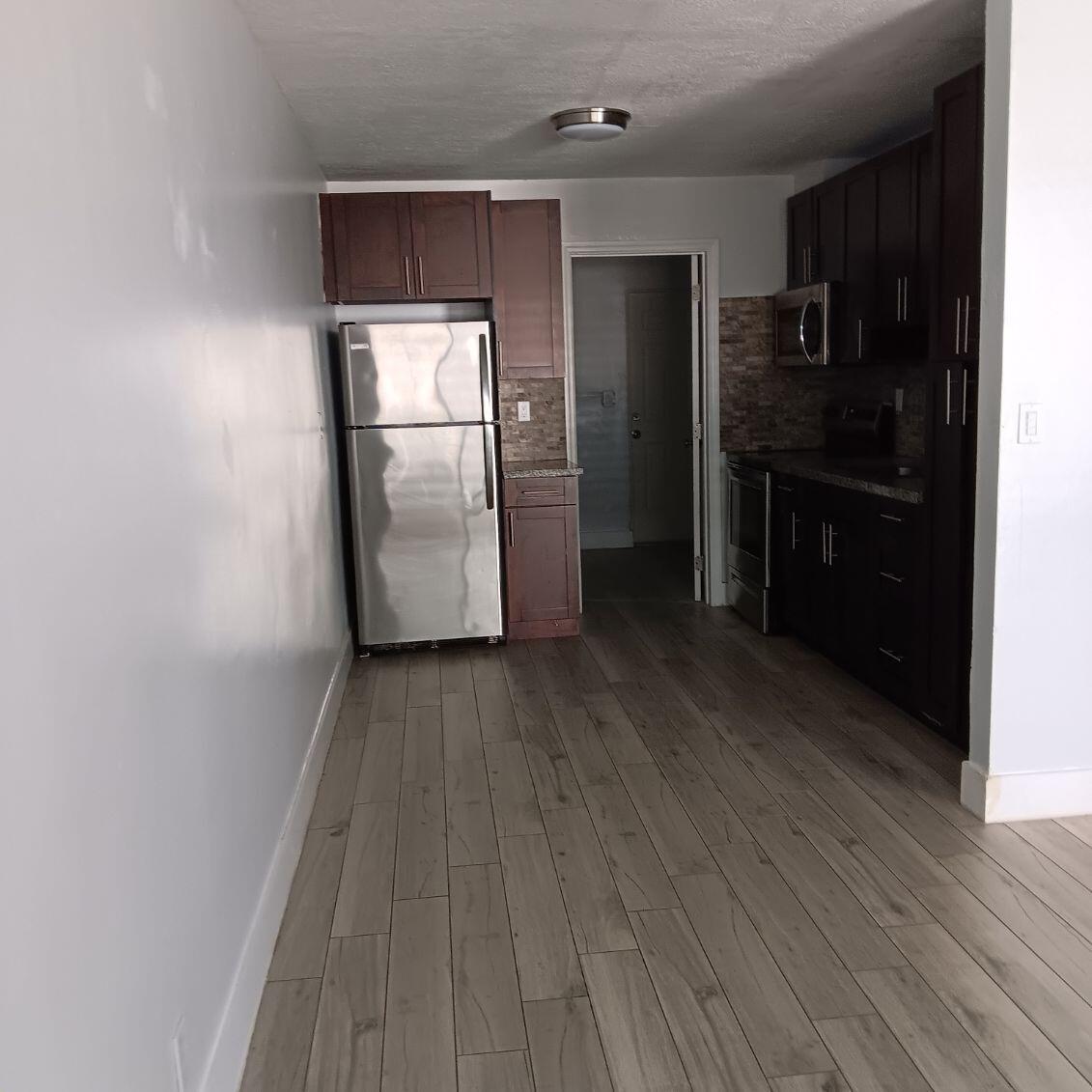 A galley kitchen features dark wood cabinets, stainless steel appliances, and light wood-look tile flooring — 4961 SW 28th Terrace # 2, Dania Beach FL 33004, DANIA BEACH, FL