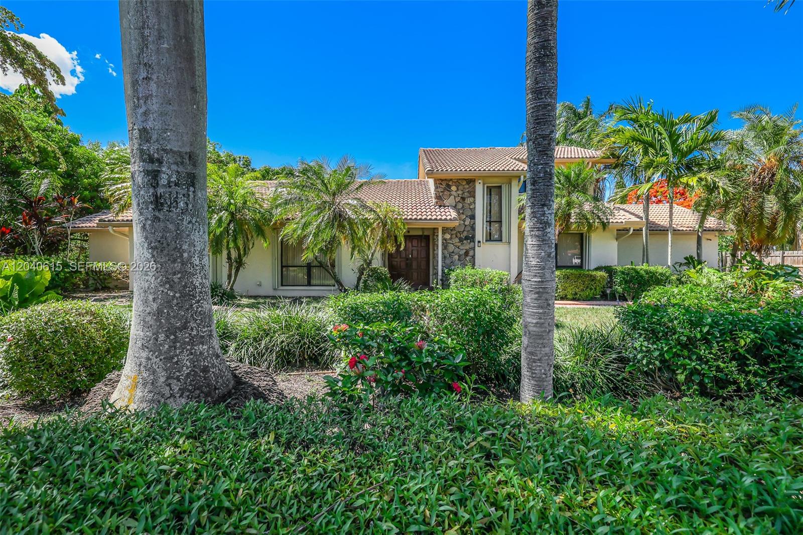 The exterior of a single-story house features a stone facade, tile roof, and palm trees — 14941 SW 164th Ter, Miami FL 33187, MIAMI, FL