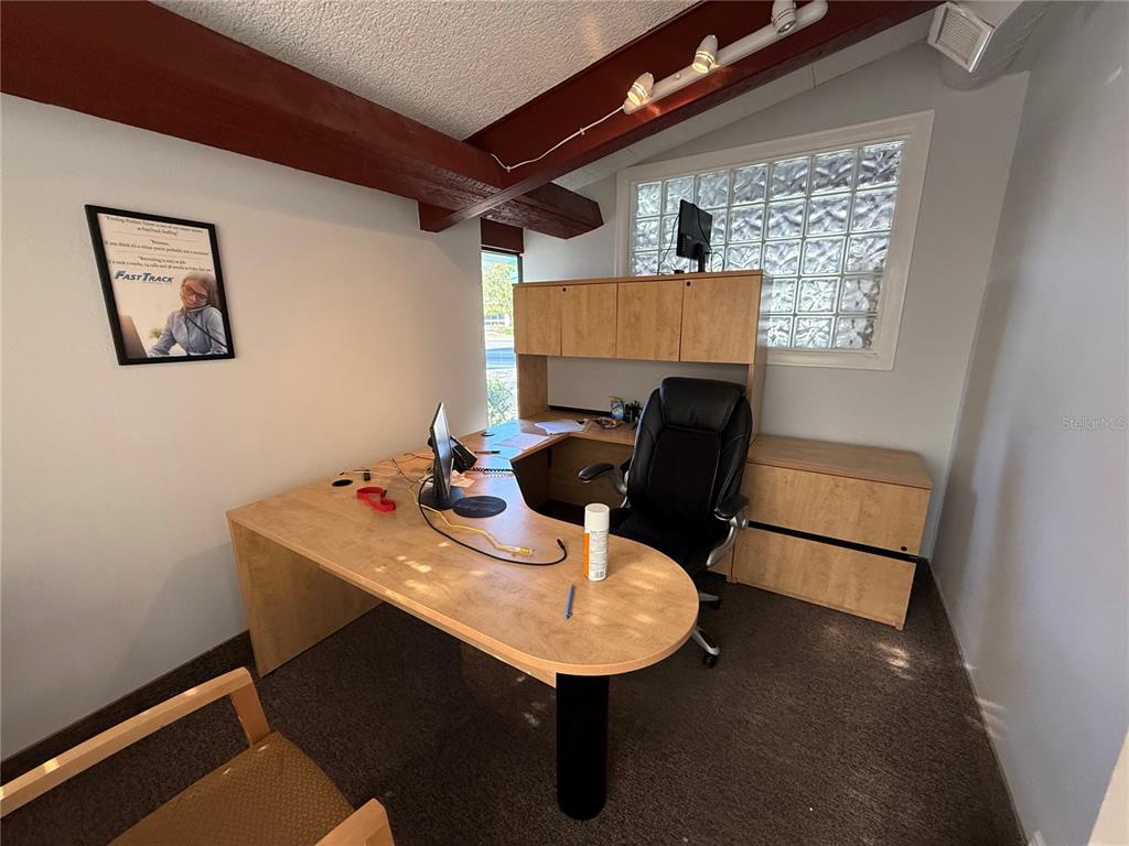 An office features a light wood L-shaped desk, a black chair, and a glass block window — 1028 E SILVER SPRINGS BOULEVARD Bldg 1, OCALA, FL