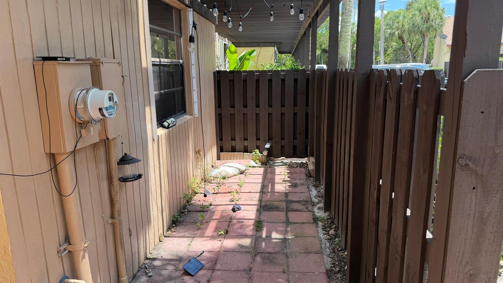 A narrow outdoor patio area features red pavers, a wooden fence, and a utility meter — 1114 NW 79th Drive, Plantation FL 33322, PLANTATION, FL