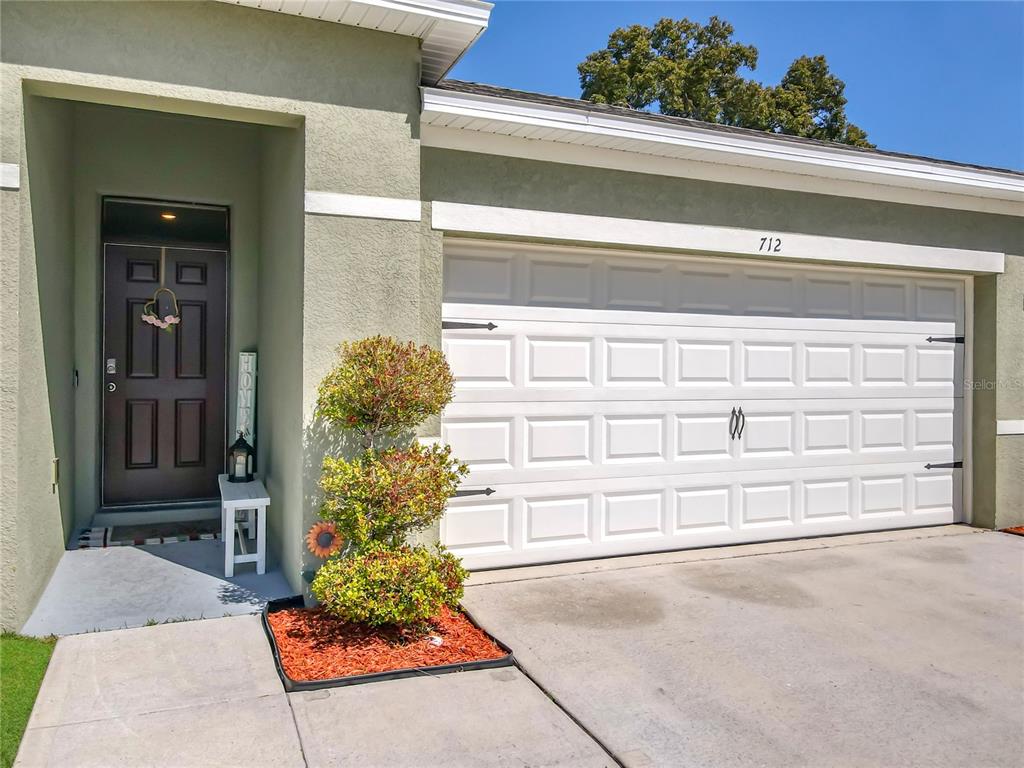 A house exterior features a white garage door, a front door, and a small garden — 712 RED HAWK LANE, DELTONA, FL