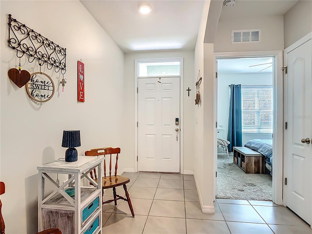 An entryway with tile flooring features a white front door, a small table, and a chair — 712 RED HAWK LANE, DELTONA, FL