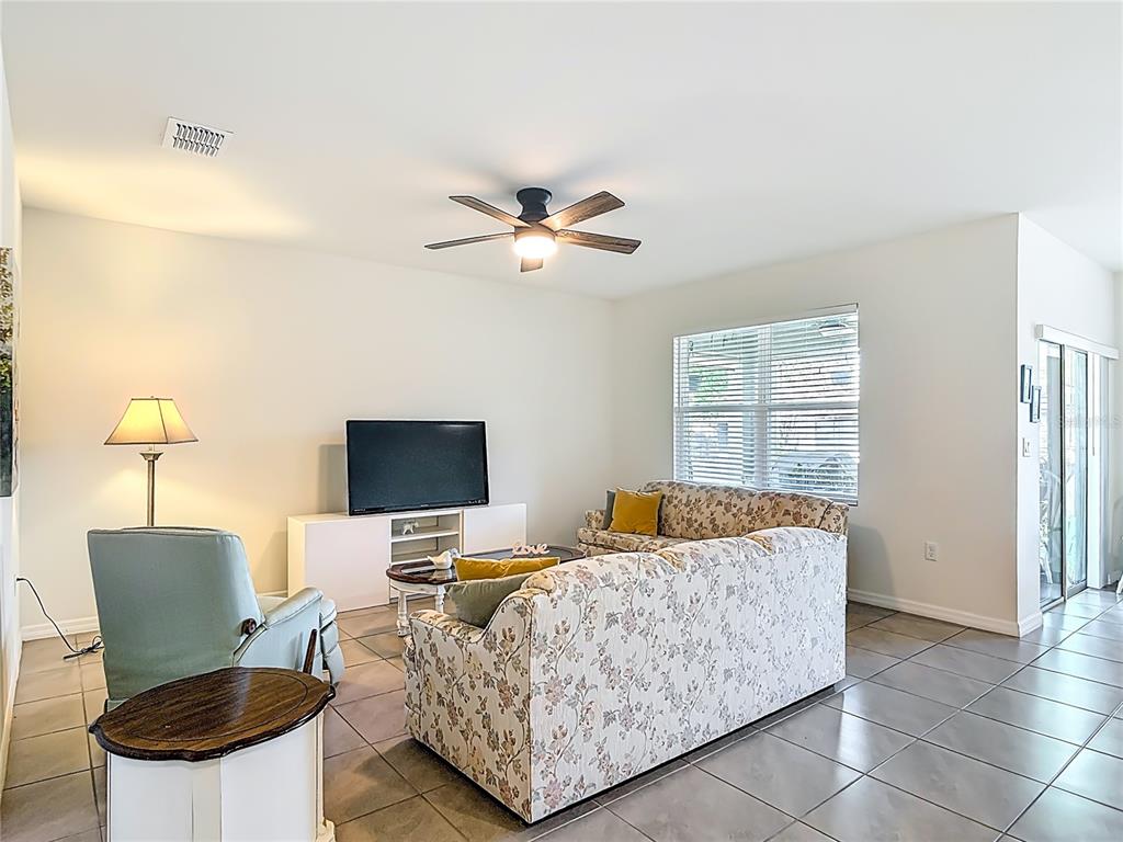 A living room features tile flooring, a floral sofa, a television console, and a ceiling fan — 712 RED HAWK LANE, DELTONA, FL