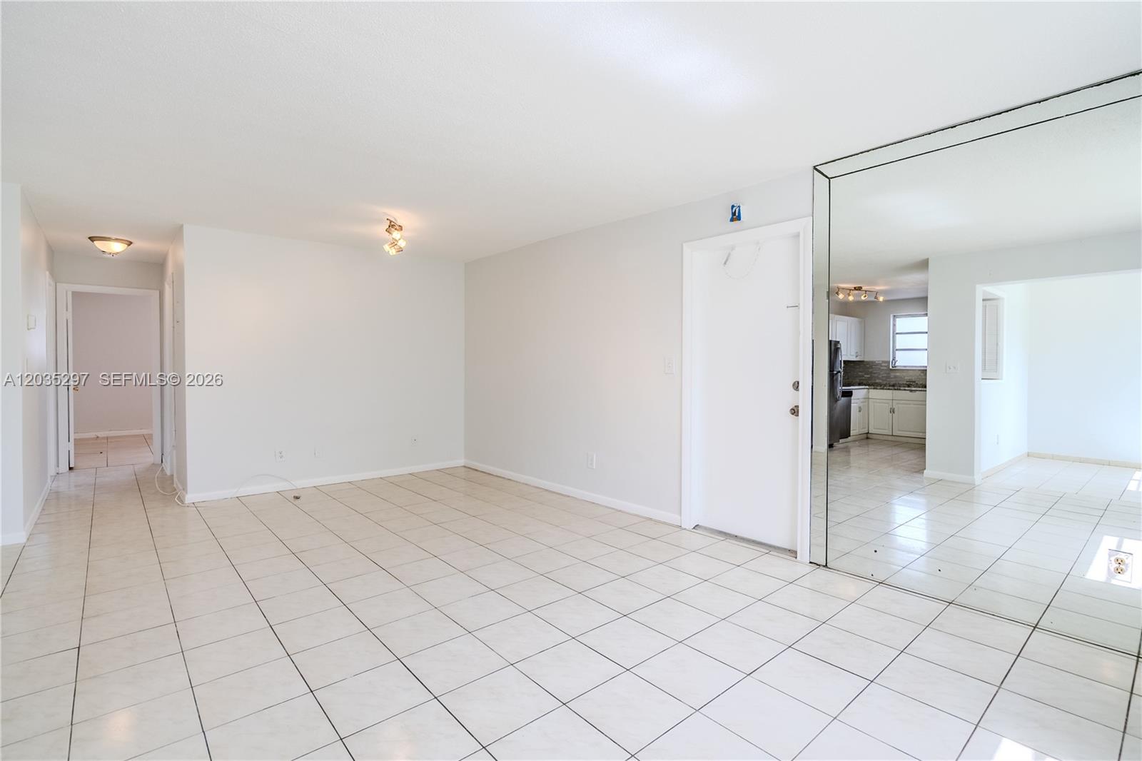 A bright, tiled living area features a mirrored wall and a doorway leading to a kitchen — 421 NE 1st St # 101, Hallandale Beach FL 33009, HALLANDALE BEACH, FL