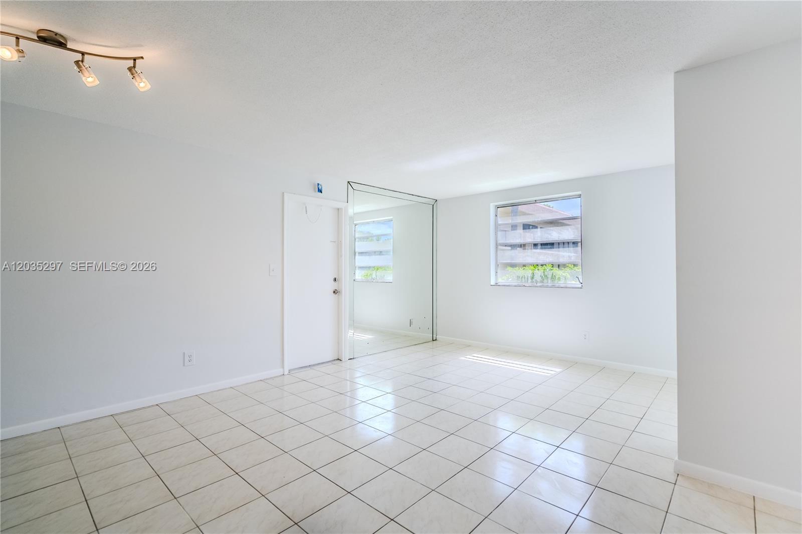 A bright, empty room features white tile flooring, a mirrored closet, and a track light — 421 NE 1st St # 101, Hallandale Beach FL 33009, HALLANDALE BEACH, FL