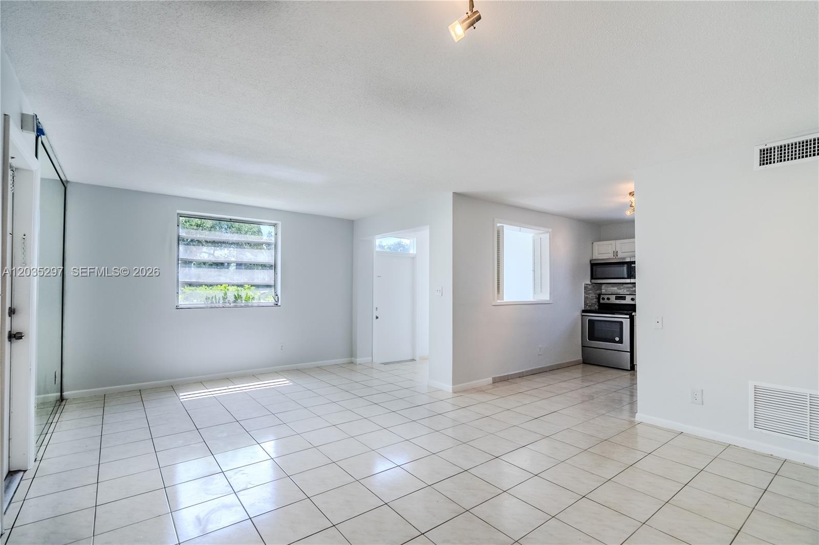 An open-concept living area features white tile flooring, a kitchen, and a window — 421 NE 1st St # 101, Hallandale Beach FL 33009, HALLANDALE BEACH, FL