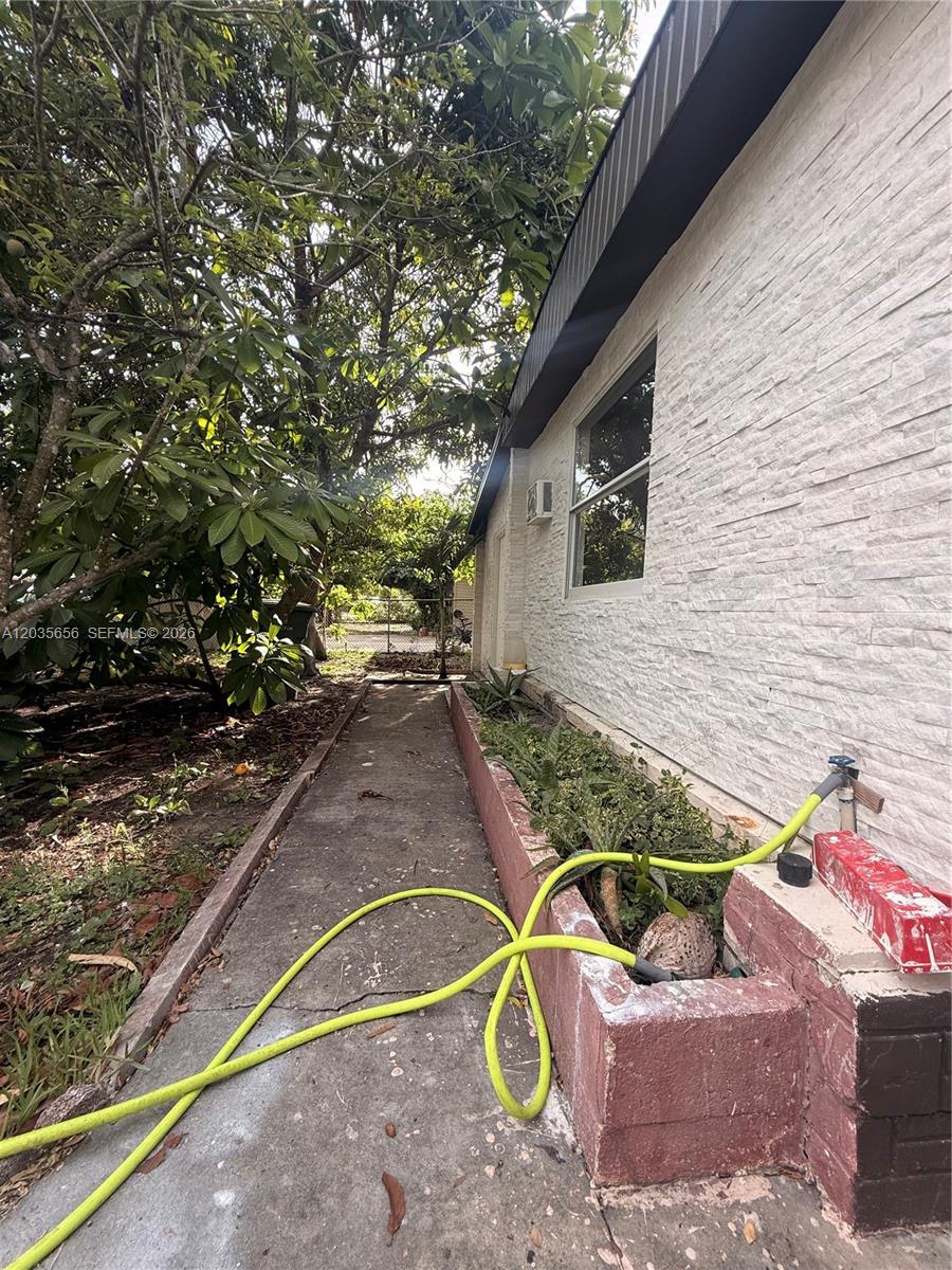 A concrete walkway runs alongside a white stone-textured exterior wall and a raised planter bed — 607 Sabal ave, Clewiston FL 33440, CLEWISTON, FL