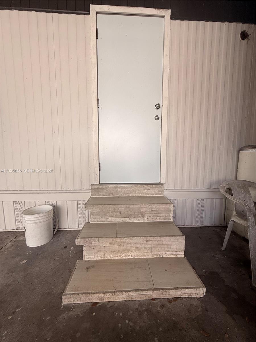 A white exterior door is accessed by three tiled steps against a vertical-paneled wall — 607 Sabal ave, Clewiston FL 33440, CLEWISTON, FL
