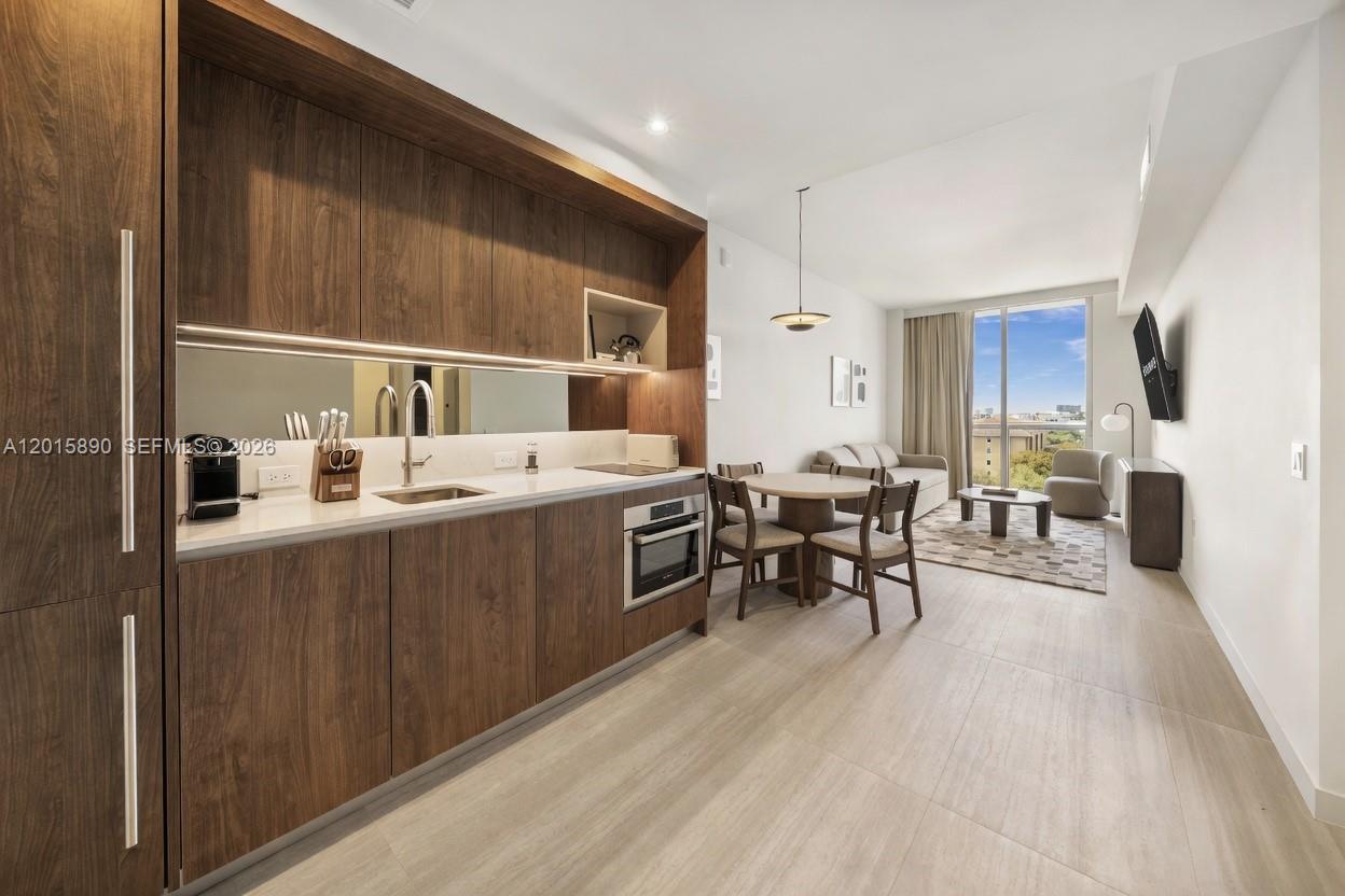 A modern kitchen with wood cabinetry and white countertops opens into a living and dining area — 1611 SW 2nd Ave # 707, Miami FL 33129, MIAMI, FL