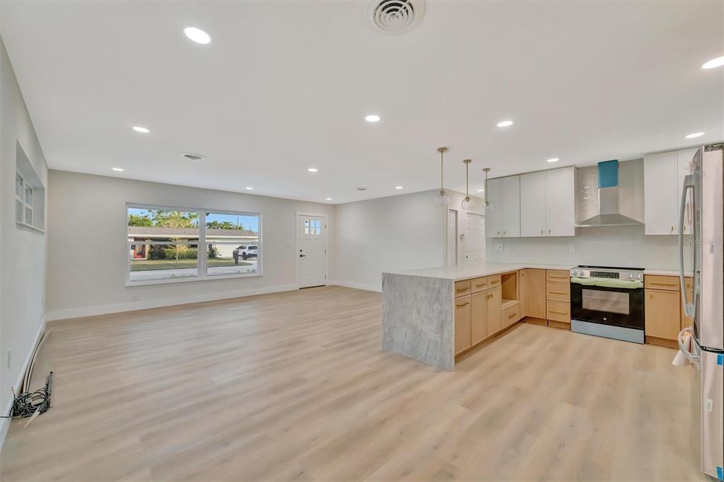 An open-concept kitchen and living area features light wood flooring and white cabinetry — 2705 SUNNYSIDE STREET, SARASOTA, FL