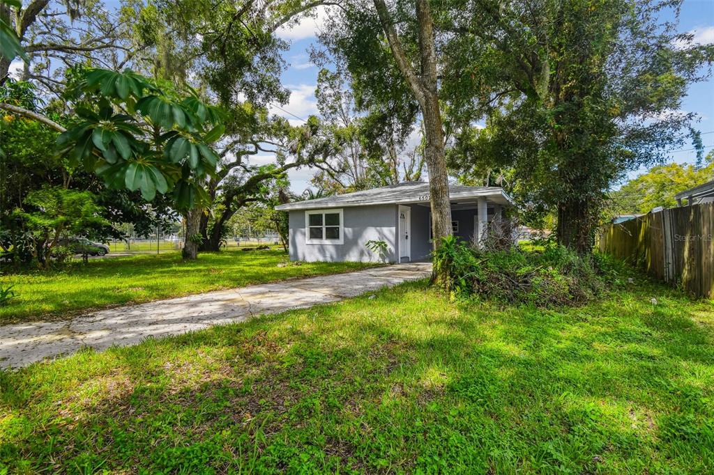 A gray single-story house with a concrete driveway sits on a grassy, tree-filled lot — 6502 N 31ST STREET, TAMPA, FL