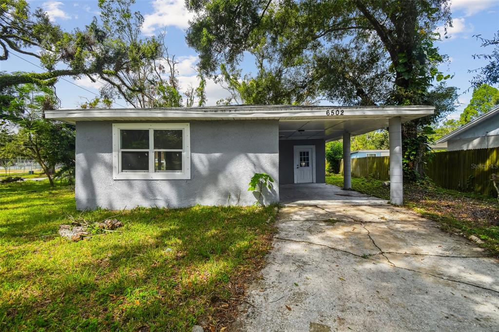 A single-story gray house features a flat roof, a front carport, and a concrete driveway — 6502 N 31ST STREET, TAMPA, FL