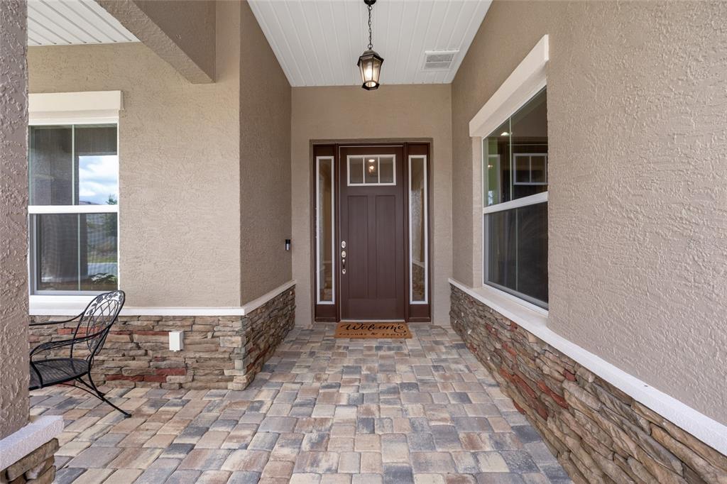 A covered entryway features a paver floor, stone siding, and a dark wood front door — 10621 SW 98TH LANE, OCALA, FL