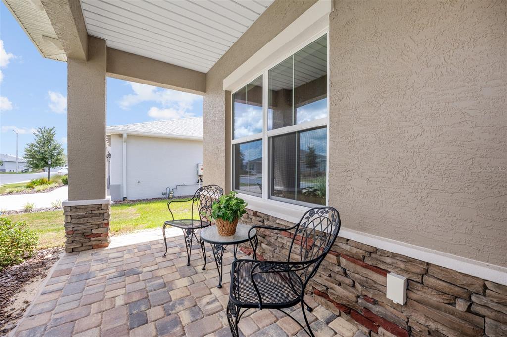A covered patio features stone veneer walls, a paver floor, and two black metal chairs — 10621 SW 98TH LANE, OCALA, FL