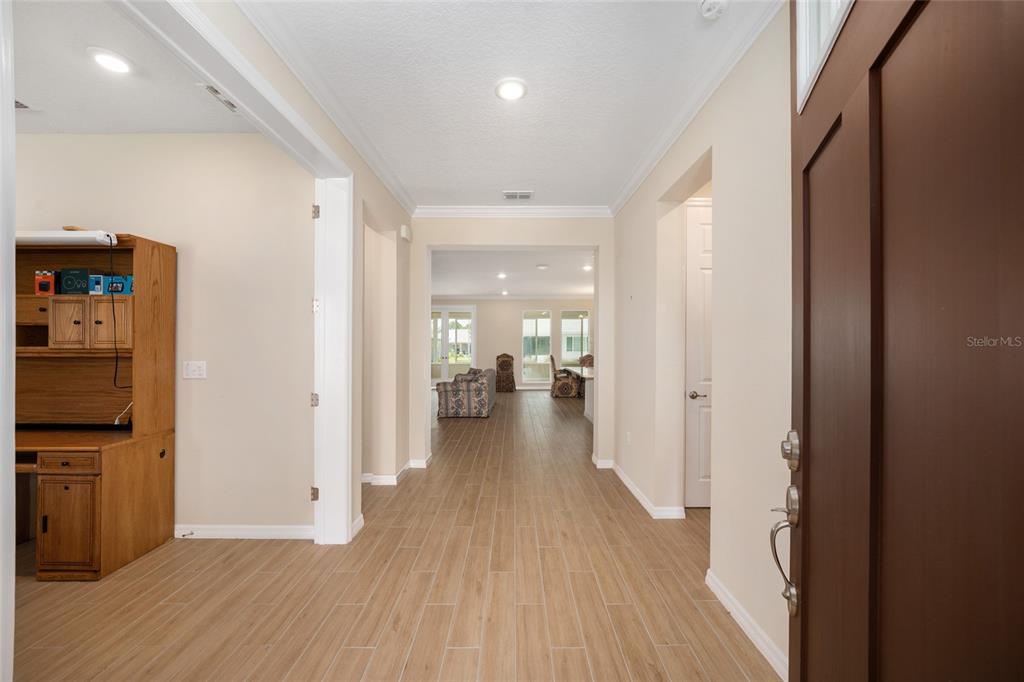 An entryway with light wood-look tile flooring leads into a living area with large windows — 10621 SW 98TH LANE, OCALA, FL