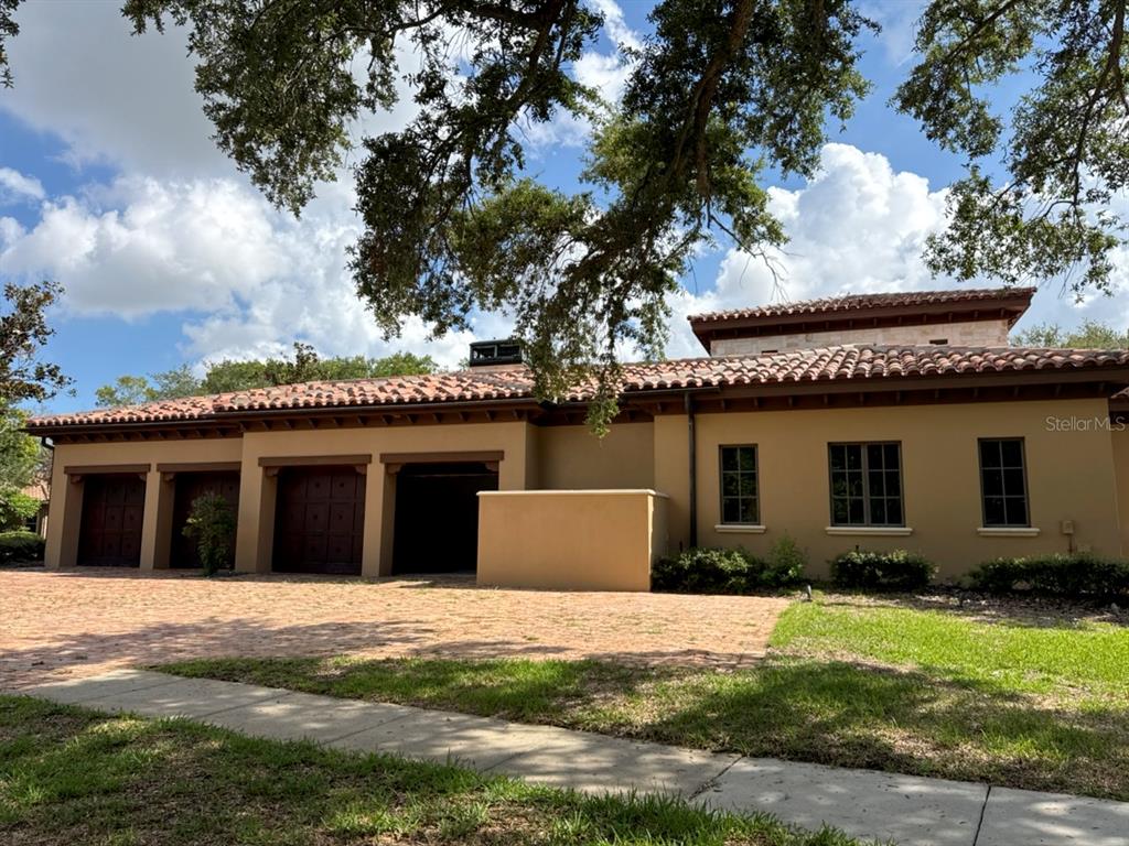 A tan house with a tile roof and a three-car garage under large oak trees — 9003 WATERASH LANE N, PINELLAS PARK, FL